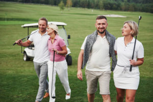 Two couples walking on golf course with golf clubs and a golf cart in the background